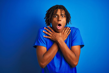 Afro american man with dreadlocks wearing t-shirt standing over isolated blue background shouting and suffocate because painful strangle. Health problem. Asphyxiate and suicide concept.