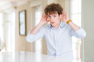 Young business man with curly read head Trying to hear both hands on ear gesture, curious for...