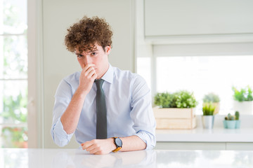 Young business man wearing a tie smelling something stinky and disgusting, intolerable smell,...