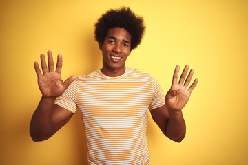 American man with afro hair wearing striped t-shirt standing over isolated yellow background...