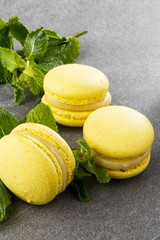 French macaroons isolated. Selective focus. Beautiful yellow macaroons with mint on gray stone background. Stylish arrangement sweet. Flat lay, top view. Macro photo.
