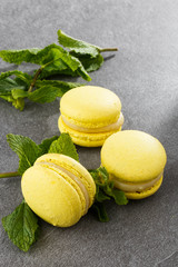 French macaroons isolated. Selective focus. Beautiful yellow macaroons with mint on gray stone background. Stylish arrangement sweet. Flat lay, top view. Macro photo.