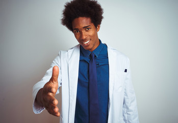 Young african american doctor man wearing coat standing over isolated white background smiling...
