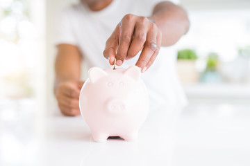 Close up of african american man saving money putting a coin inside piggy bank