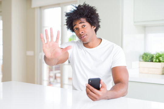 African American man using smartphone with open hand doing stop sign with serious and confident expression, defense gesture