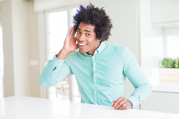 African American business man wearing elegant shirt smiling with hand over ear listening an hearing to rumor or gossip. Deafness concept.