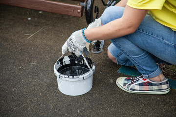 Girl paints a bench in the park. Work with paint. Time to upgrade the garden. Girl with a brush in...