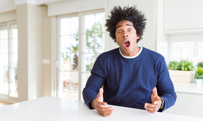 Young african american man wearing casual sweater sitting at home In shock face, looking skeptical...