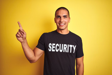 Young safeguard man with security t-shirt over yellow isolated background very happy pointing with...