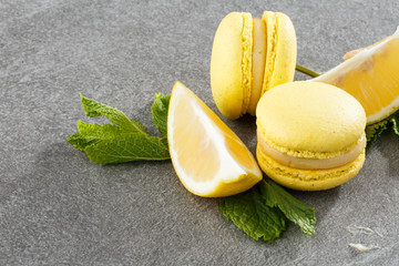 French macaroons isolated. Selective focus. Beautiful yellow macaroons with lemon and mint on gray stone background. Stylish arrangement sweet. Flat lay, top view. Macro photo.