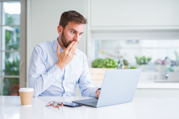 Handsome man working using computer laptop and drinking a cup of coffee cover mouth with hand shocked with shame for mistake, expression of fear, scared in silence, secret concept