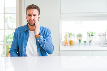 Handsome man at home touching mouth with hand with painful expression because of toothache or dental illness on teeth. Dentist concept.