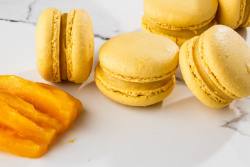 French macaroons isolated. Selective focus. Beautiful yellow macaroons with sliced mango on marble background. Stylish arrangement sweet. Flat lay, top view. Macro photo. With copy space.