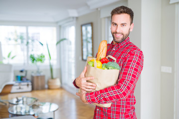 Handsome man holding paper bag full of fresh groceries at home