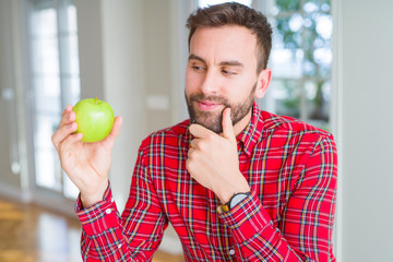Handsome man eating fresh healthy green apple serious face thinking about question, very confused idea