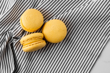 French macaroons isolated. Selective focus. Beautiful yellow macaroons on striped napkin background. Stylish arrangement sweet. Flat lay, top view. Macro photo.