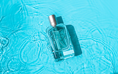 Transparent glass cosmetic perfume bottle in the blue water . Top view