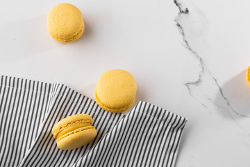 French macaroons isolated. Selective focus. Beautiful yellow macaroons in striped napkin on marble background. Stylish arrangement sweet. Flat lay, top view. Macro photo. With copy space.