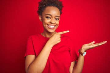 Young beautiful african american woman with afro hair over isolated red background amazed and smiling to the camera while presenting with hand and pointing with finger.