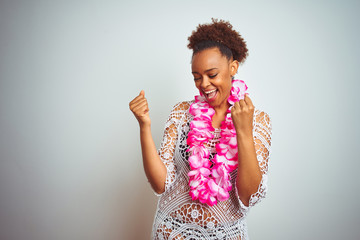 Young african american woman with afro hair wearing flower hawaiian lei over isolated background very happy and excited doing winner gesture with arms raised, smiling and screaming for success. 