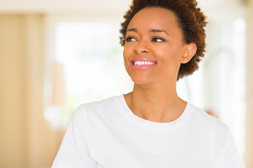 Young beautiful african american woman wearing casual white t-shirt looking away to side with smile on face, natural expression. Laughing confident.