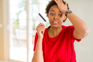 Young african american woman holding credit card stressed with hand on head, shocked with shame and surprise face, angry and frustrated. Fear and upset for mistake.