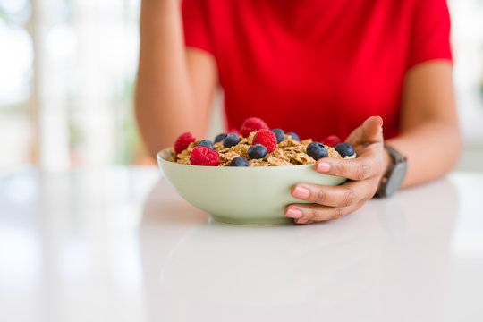 Close up of young woman eating healthy cereals and berries for breakfast
