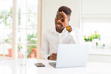 African american business man working using laptop doing ok gesture with hand smiling, eye looking through fingers with happy face.