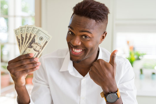 African american man holding twenty dollars bank notes happy with big smile doing ok sign, thumb up with fingers, excellent sign