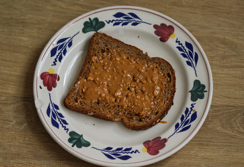 Bread with peanut butter on white plate on wooden background