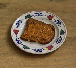 Bread with peanut butter on white plate on wooden background