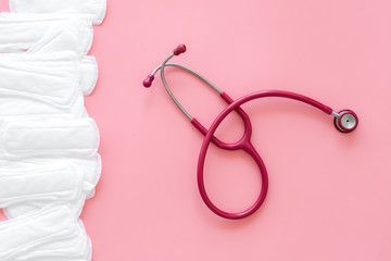 Gynaecologist and menstruation concept with stethoscope and sanitary pads on pink background top view