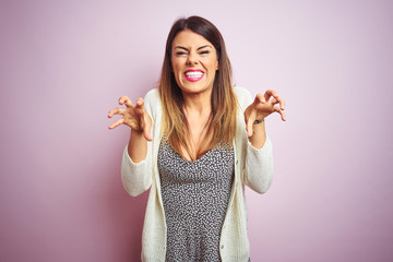 Young beautiful woman standing over pink isolated background smiling funny doing claw gesture as...