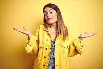 Young beautiful woman wearing denim jacket standing over yellow isolated background clueless and...