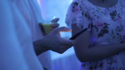 Young man with a phone in his hand at a party in a nightclub. Looks at the phone. Uses the Internet in the phone. Light from the screen of the smartphone