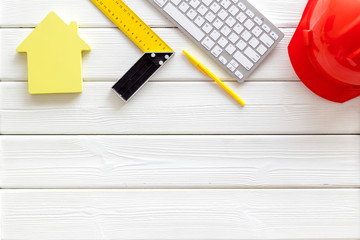 Constructor office desk with tools, helmet, ruler, keyboard and house figure on white wooden background top view mock up