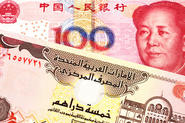 A red, Chinese one hundred yuan renminbi bank note with a five dirham bank note from the United Arab Emirates close up in macro