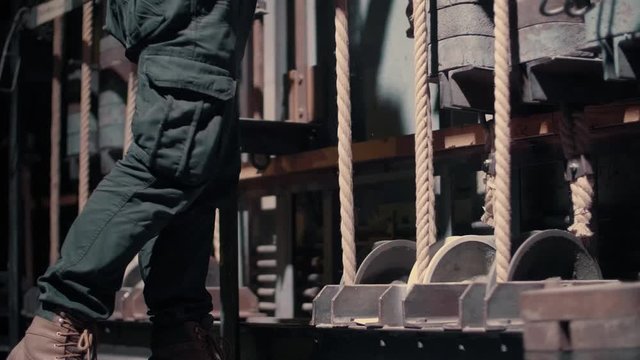Man pulls the rope in theatre backstage. Details of the iron rolls which hold the ropes and spin when the man pulls the rope.