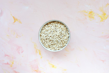 Uncooked oatmeal or oat flakes in a bowl on a pink background