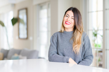 Young beautiful woman wearing winter sweater at home winking looking at the camera with sexy...