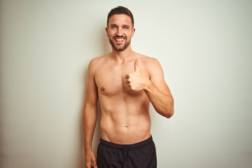 Young handsome shirtless man over isolated background doing happy thumbs up gesture with hand. Approving expression looking at the camera showing success.