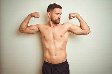 Fototapeta premium Young handsome shirtless man over isolated background showing arms muscles smiling proud. Fitness concept.