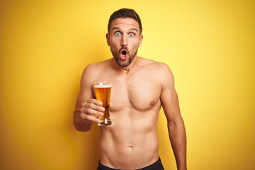 Fototapeta premium Young handsome shirtless man drinking a pint of beer over isolated yellow background scared in shock with a surprise face, afraid and excited with fear expression