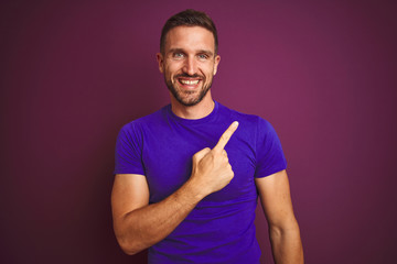 Young man wearing casual purple t-shirt over lilac isolated background cheerful with a smile of face pointing with hand and finger up to the side with happy and natural expression on face