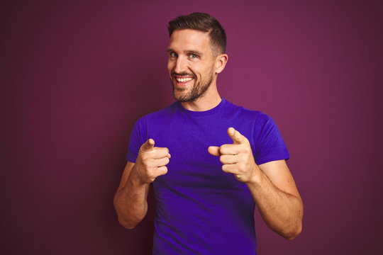 Young man wearing casual purple t-shirt over lilac isolated background pointing fingers to camera with happy and funny face. Good energy and vibes.