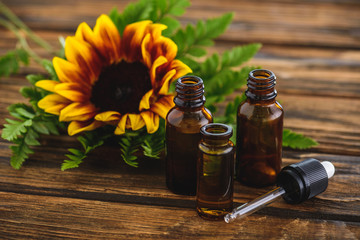 sunflower, fern leaves, bottles with essential oils and dropper on wooden surface