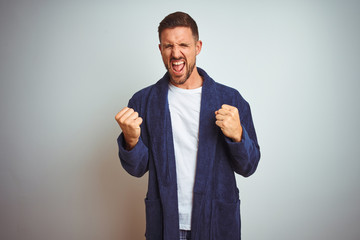 Young man wearing comfortable pajamas and robe at morning over isolated background very happy and excited doing winner gesture with arms raised, smiling and screaming for success. Celebration concept.