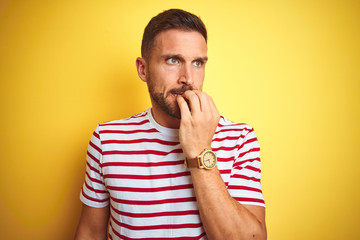 Young handsome man wearing casual red striped t-shirt over yellow isolated background looking...