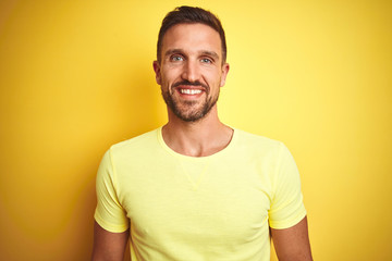 Young handsome man wearing casual yellow t-shirt over yellow isolated background with a happy and cool smile on face. Lucky person.
