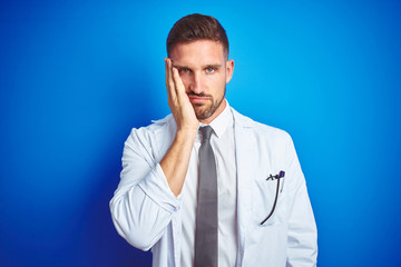 Young handsome doctor man wearing white professional coat over isolated background thinking looking...